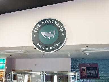 A round sign with a fish logo and the words The Boatyard Fish and Chips above a counter in a restaurant at Billing Aquadrome Holiday Park