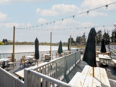 An outdoor seating area with tables umbrellas string lights and a view of a lake at Starlight Skylight - Billing Aquadrome