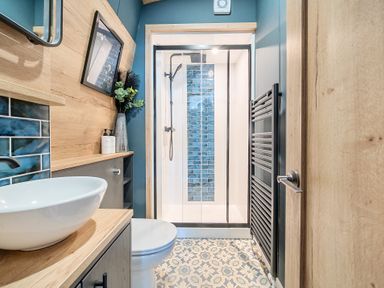 A bathroom with a white sink, toilet, glass shower enclosure, blue tiles, and patterned floor at Starlight Skylight - Billing Aquadrome Holiday Park