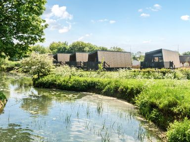 A row of modern wooden cabins near a waterway with lilies and green vegetation at Celestial Skylight - Billing Aquadrome in Billing Aquadrome Holiday Park