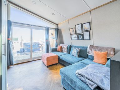 A living room with a blue sectional sofa orange ottoman and framed pictures above at Celestial Skylight - Billing Aquadrome in Billing Aquadrome Holiday Park