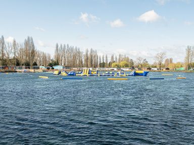 An inflatable water obstacle course on a lake with trees and buildings in the background at Aquadrome Abode Billing Aquadrome Holiday Park
