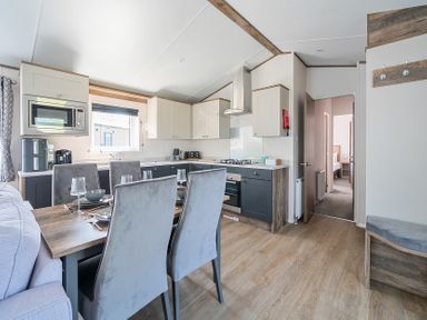A kitchen and dining area with a table set with plates and glasses and grey chairs at Aquadrome Abode - Billing Aquadrome Holiday Park