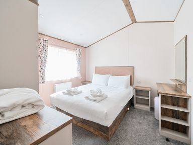 A bedroom with a double bed towels on bed bedside tables window with curtains and a dressing table at Aquadrome Abode - Billing Aquadrome