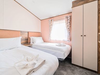 A bedroom with two single beds a window with patterned curtains and a wardrobe at Aquadrome Abode - Billing Aquadrome Holiday Park