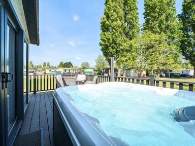 An outdoor deck with a hot tub and wicker chairs surrounded by trees and homes at Aquadrome Abode Billing Aquadrome Holiday Park