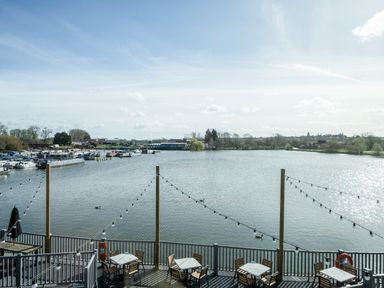 A lakeside view with boats docked in the marina and tables with chairs on a deck overlooking the water at Lakeside Lullaby Billing Aquadrome