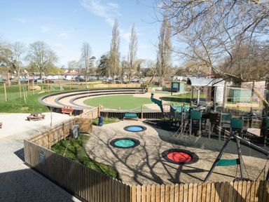 An outdoor playground with trampolines swings climbing structures and circular tiered seating at Lakeside Lullaby Billing Aquadrome