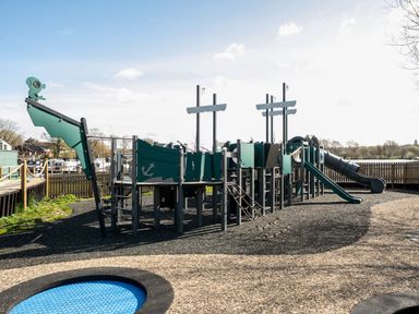 An outdoor playground structure shaped like a ship with slides and climbing nets at Lakeside Lullaby - Billing Aquadrome in Billing Aquadrome Holiday Park