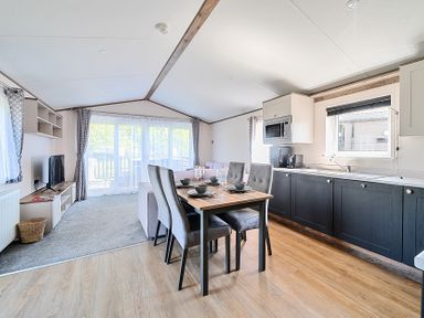 An open plan living area with a dining table and chairs kitchen cabinets and a sitting area with a TV at Lakeside Lullaby - Billing Aquadrome in Billing Aquadrome Holiday Park