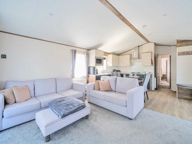 A living area with two sofas, an ottoman, and a kitchen with dining table and chairs at Lakeside Lullaby - Billing Aquadrome