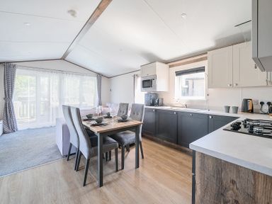 A kitchen and dining area with a wooden dining table set for four chairs and kitchen cabinets at Lakeside Lullaby  Billing Aquadrome Holiday Park