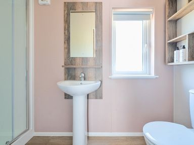 A bathroom with a pedestal sink mirror window shelving and a toilet at Lakeside Lullaby Billing Aquadrome Holiday Park