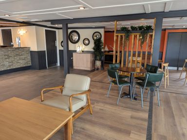 A seating area with tables and chairs including a beige armchair near a coffee counter in a lounge at Lakeside Lullaby - Billing Aquadrome Holiday Park