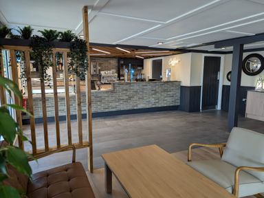 An indoor seating area with chairs a wooden table and a wooden partition next to a counter with coffee equipment and taps at Lakeside Lullaby - Billing Aquadrome Holiday Park