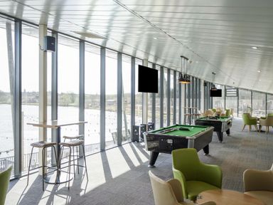 A recreational room with pool tables, chairs, tables, and large windows overlooking water at Moonlit Skylight - Billing Aquadrome