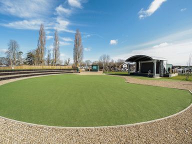 An outdoor amphitheater area with a small stage and tiered seating surrounded by gravel paths at Moonlit Skylight - Billing Aquadrome in Billing Aquadrome Holiday Park