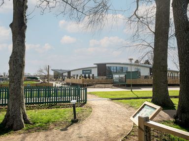 A green fenced park area with trees and a gravel path leading to a building labeled The Venue at Billing Aquadrome Holiday Park