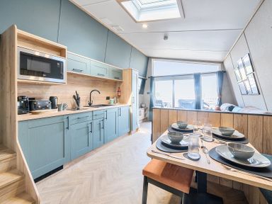 A kitchen and dining area with blue cabinets, a wooden dining table set for four, and large windows at Moonlit Skylight - Billing Aquadrome in Billing Aquadrome Holiday Park