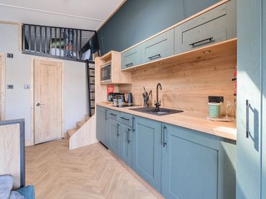 A kitchen with blue cabinets wooden countertop a sink microwave coffee maker utensils and stairs leading to a loft bed at Moonlit Skylight - Billing Aquadrome in Billing Aquadrome Holiday Park