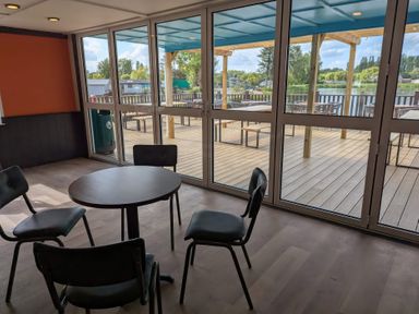 A seating area with four chairs around a round table next to large glass doors overlooking a deck with tables and chairs at Moonlit Skylight - Billing Aquadrome