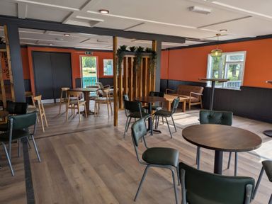 A dining area with round tables and chairs with orange and black walls and windows at Moonlit Skylight - Billing Aquadrome