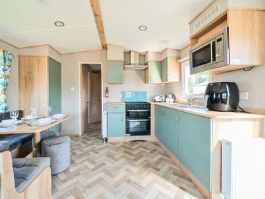 A kitchen with green and wood cabinets a black oven and microwave a dining table set with plates and wine glasses at Brookside Bliss Billing Aquadrome Holiday Park