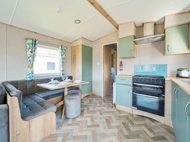 A kitchen and dining area with green cabinets a stove and a corner sofa with a table at Brookside Bliss - Billing Aquadrome in Billing Aquadrome Holiday Park