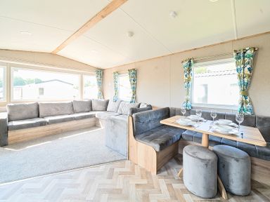 A living room with an L-shaped sofa and a dining table with place settings at Brookside Bliss - Billing Aquadrome in Billing Aquadrome Holiday Park