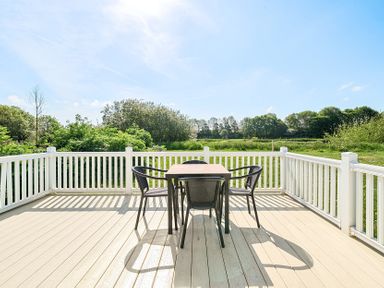 An outdoor deck with a table and four chairs surrounded by white railing and greenery at Island Breeze - Hayling Island Hayling Island Holiday Park