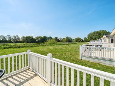 View of multiple outdoor decks with white railings facing a grassy area and trees at Island Breeze - Hayling Island in Hayling Island Holiday Park