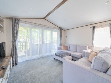 A living room with two sofas a footstool a television and large windows with curtains at Wave Whisperers - Hayling Island in Hayling Island Holiday Park