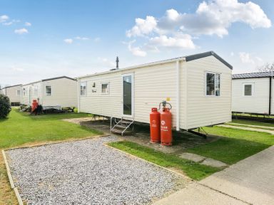 A row of white mobile homes with propane tanks on grass at The Lookout - Hayling Island in Hayling Island Holiday Park