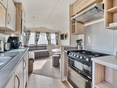 A kitchen and living area with a stove microwave sofa and windows at The Lookout - Hayling Island in Hayling Island Holiday Park