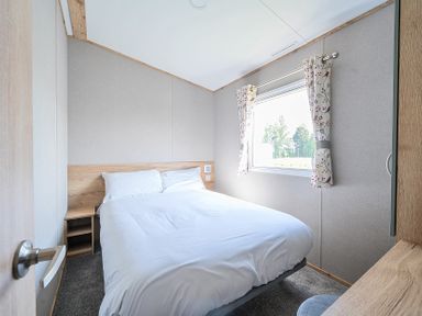 A bedroom with a double bed beside a window with curtains at Sunset Sands - Hayling Island in Hayling Island Holiday Park