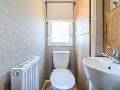 A small bathroom with a toilet radiator sink and window at Sunset Sands - Hayling Island Hayling Island Holiday Park