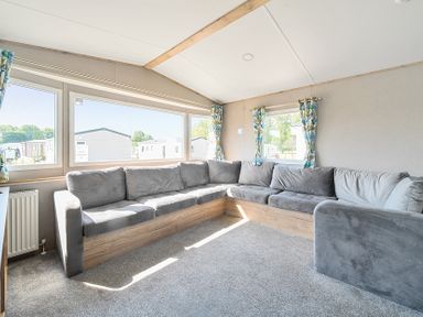 A living room with a large gray corner sofa and windows with floral curtains at Sunset Sands - Hayling Island in Hayling Island Holiday Park