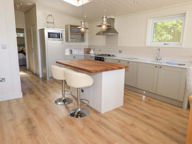 A kitchen with a wooden island countertop two white stools a microwave gas stove and window at Kingfisher Lodge in Gargrave