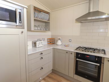 A kitchen corner with a microwave oven plates glasses a toaster a kettle and a gas stove with an oven at Kingfisher Lodge in Gargrave