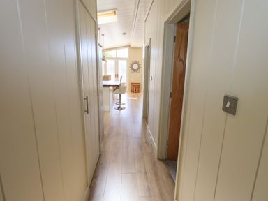 A hallway with wooden floor leading to a dining area with chairs and a mirror on the wall at Kingfisher Lodge in Gargrave