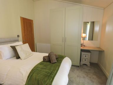 A bedroom with a bed, wardrobe, desk with lamp and mirror at Kingfisher Lodge in Gargrave
