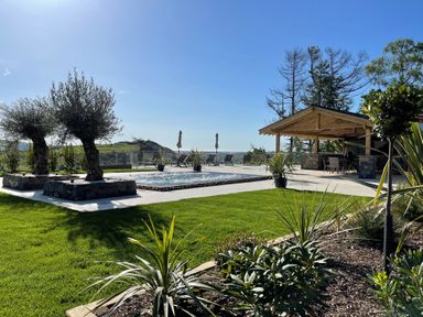 An outdoor space with a swimming pool surrounded by plants and trees and a covered seating area at Forest View in Pontyclun