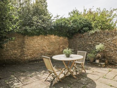 A garden with a stone wall and a table with chairs at Stable cottage Sopworth near Sherston