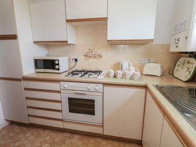 A kitchen with a microwave, gas stove, oven, kettle, and cups at Flat 9 Swanage