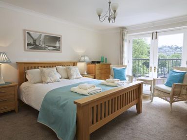 A bedroom with a wooden bed blue bedding two wicker chairs with blue cushions and glass doors at 10 Dartmouth House in Dartmouth