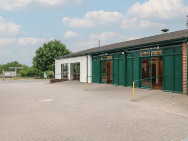 An information centre building with green doors and windows and a paved area outside at Sycamore Lodge in Rosliston