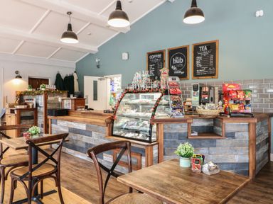 A cafe counter with a display case of snacks and drinks with tables and chairs in front at Sycamore Lodge in Rosliston