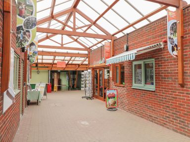 A covered corridor with brick walls and wooden beams with a reception and shop area at Sycamore Lodge in Rosliston