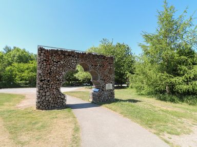 A path passing through an archway made of stacked logs in a park with trees at Sycamore Lodge in Rosliston