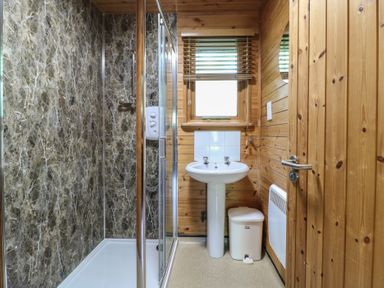 A bathroom with a shower enclosure a sink a window a bin and wooden walls at Cedar Lodge in Rosliston